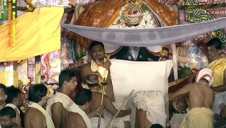 Servitors holding a new cloth in front of Lord Jagannath during offering of Adhara Pana